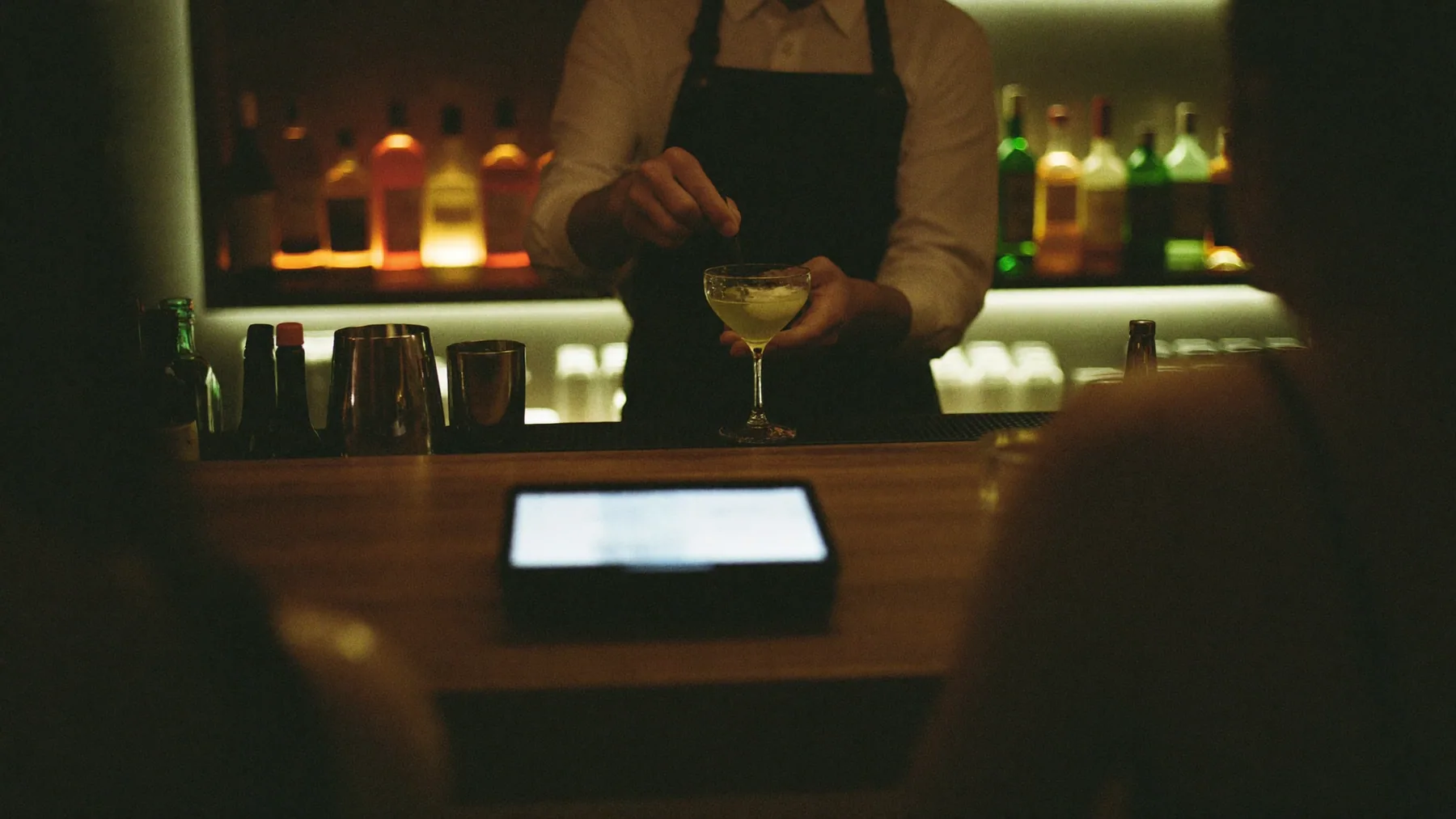 Bartender terminando un trago en la barra de un bar, con la tablet de cobro apoyada al borde