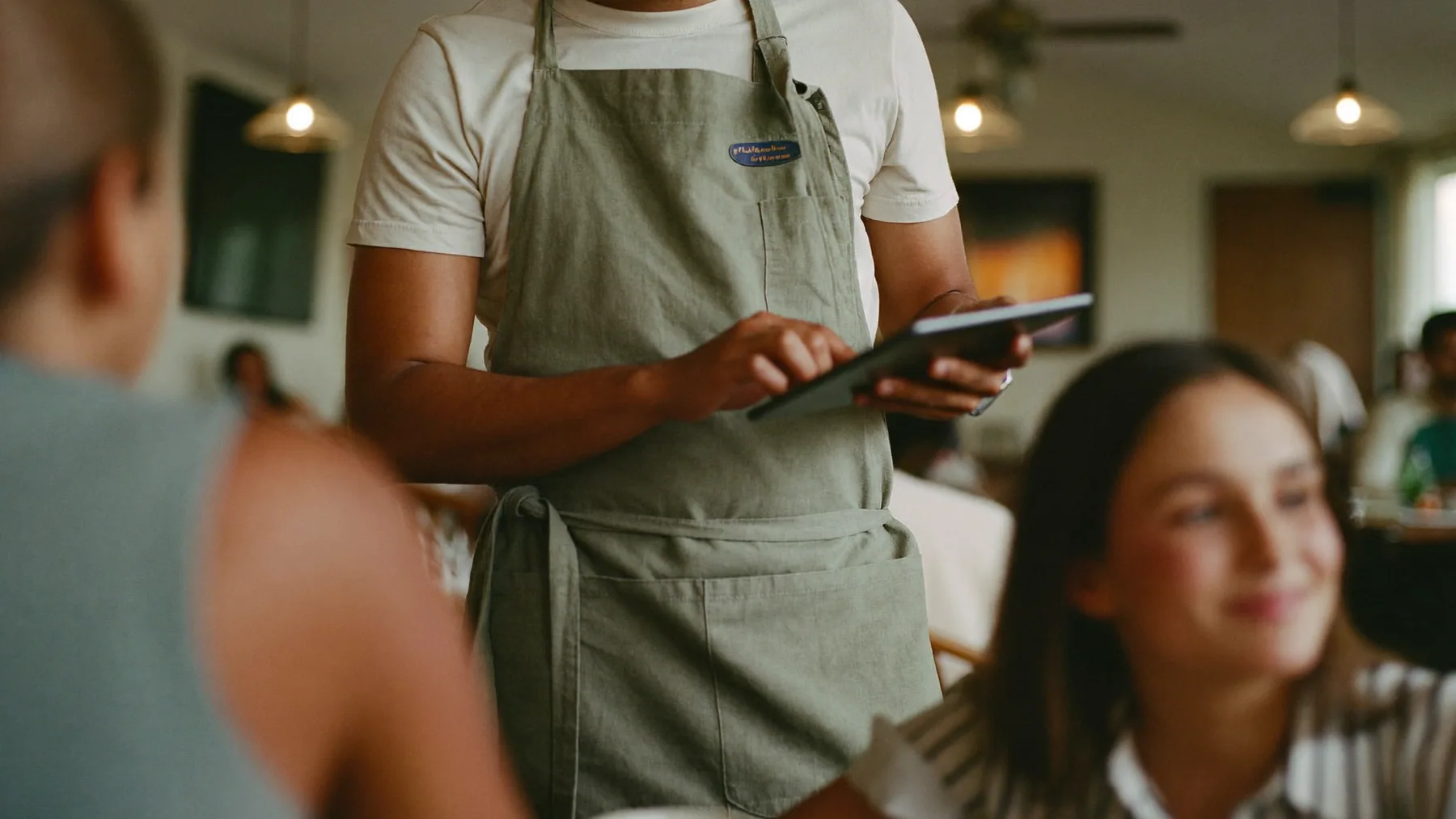 Mozo tomando el pedido en una tablet en el salón lleno de un restaurante