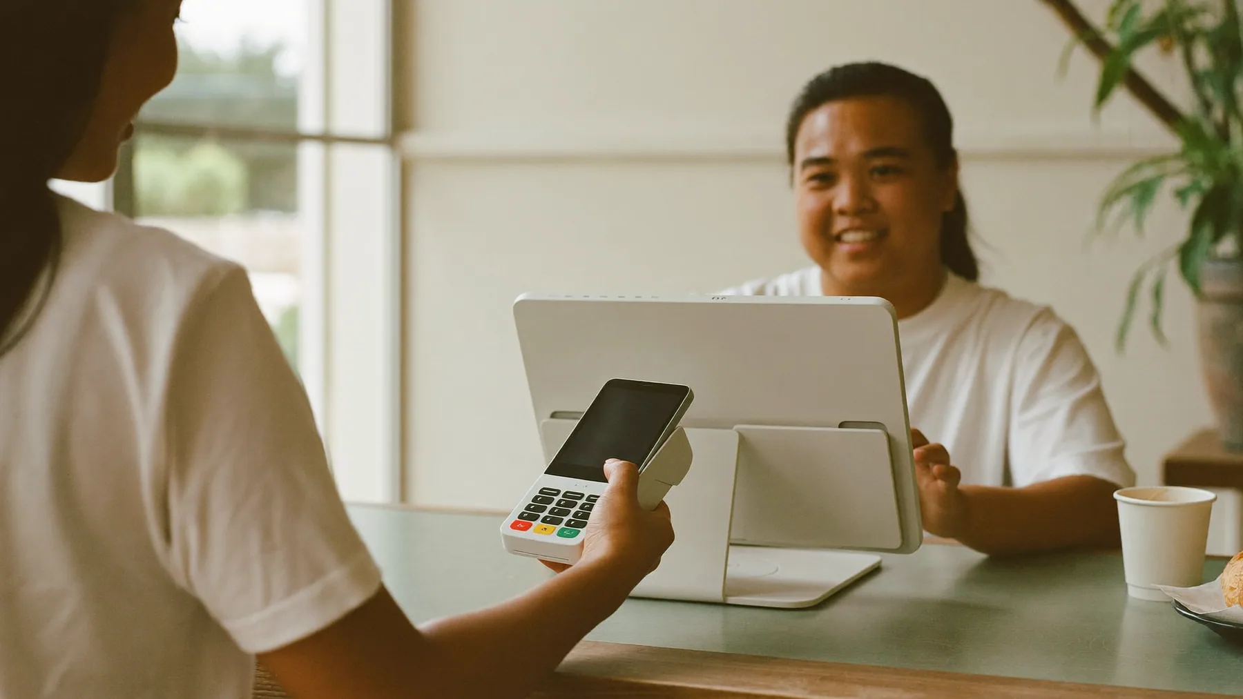 Cliente pagando con el celular en un lector contactless en el mostrador de una cafetería