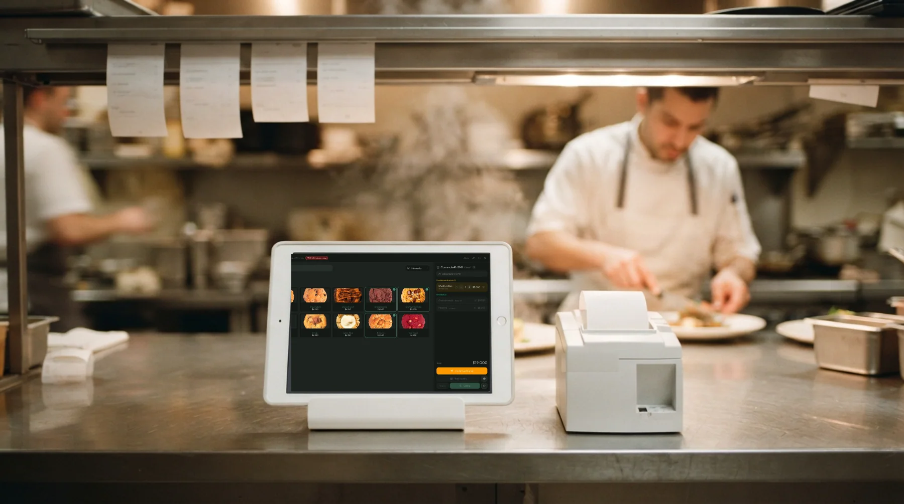 Tablet en el pase de la cocina con la comanda de Mellysoft en pantalla, junto a la impresora de comandas y el cocinero emplatando