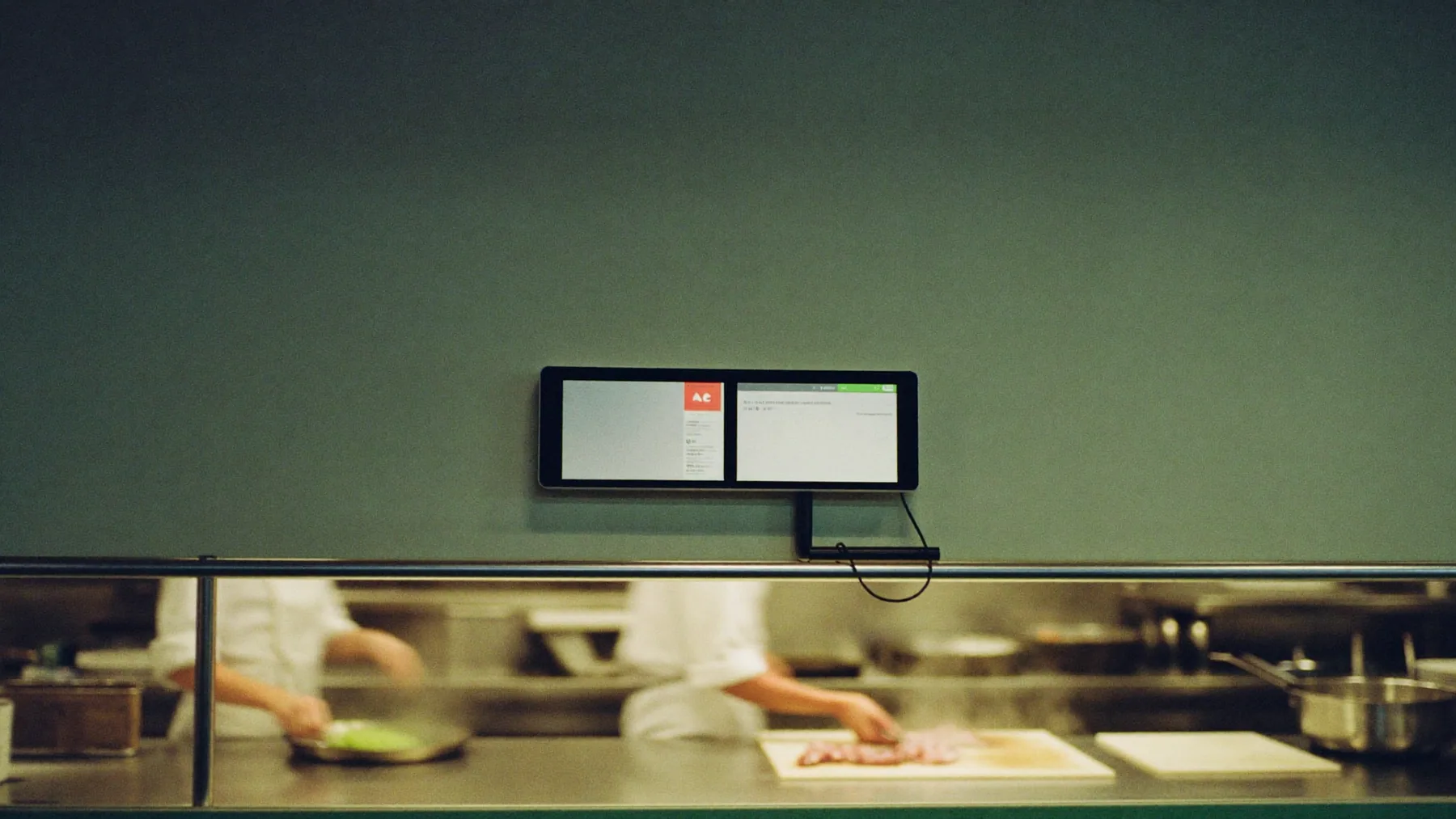 Pantalla de cocina montada en la pared sobre la línea, con dos cocineros trabajando