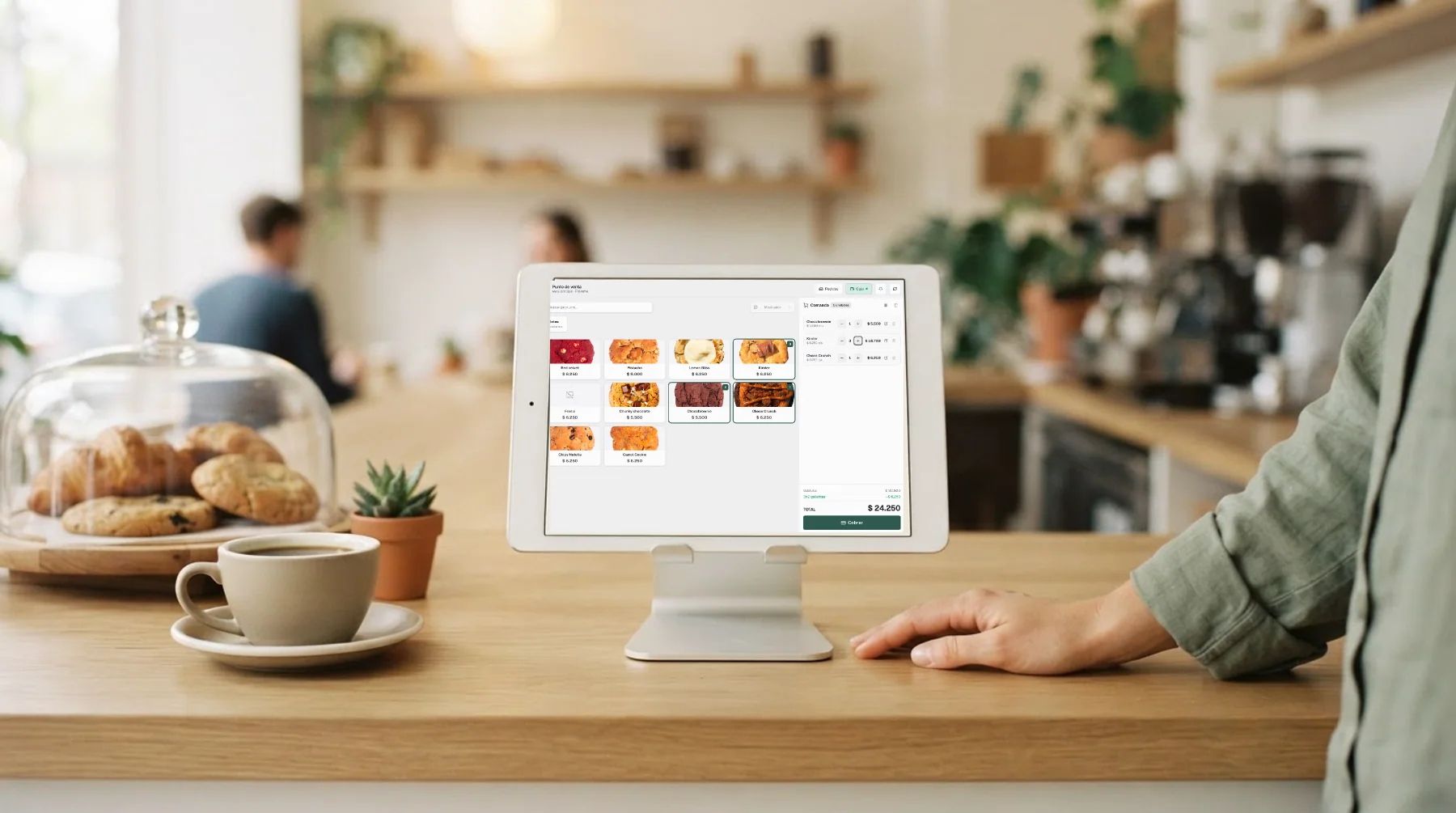 Tablet con el POS web de Mellysoft sobre el mostrador de una cafetería: grilla de galletitas con foto y precio, y la comanda a la derecha