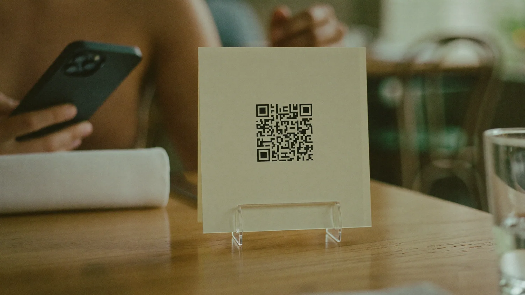 Atril con el código QR de la carta sobre la mesa de un restaurante y un cliente con el celular en la mano